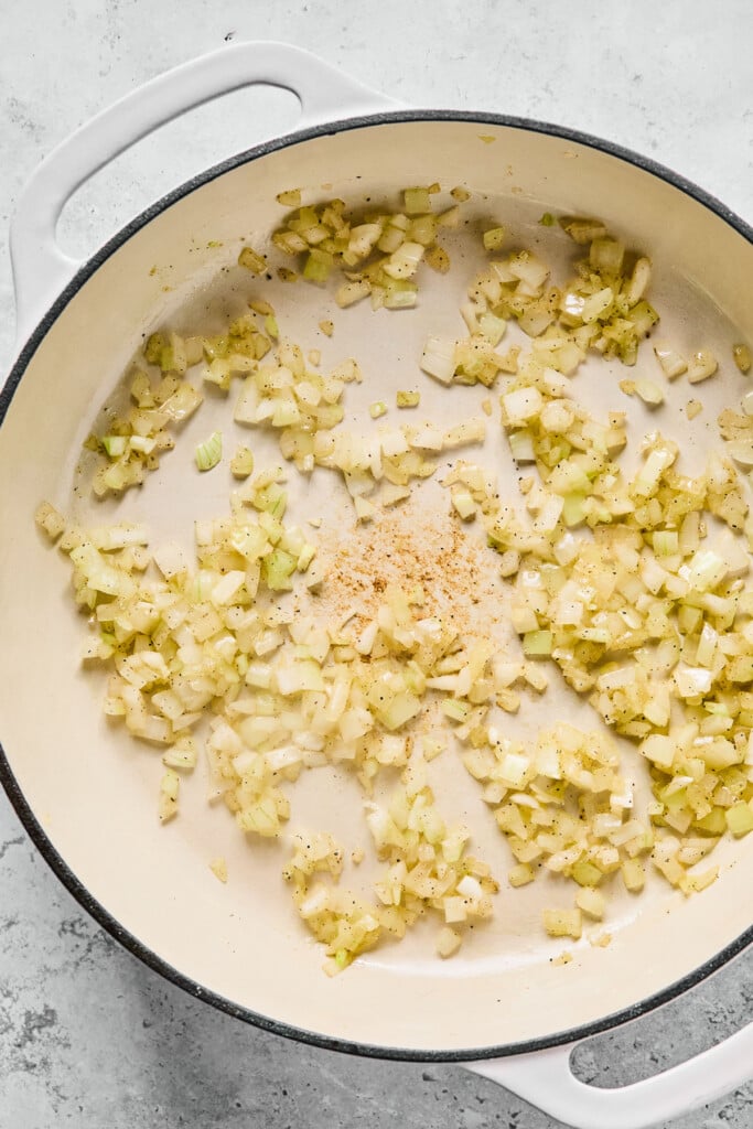 Large white dutch oven filled with sautéed diced onions with minced garlic on top of them.
