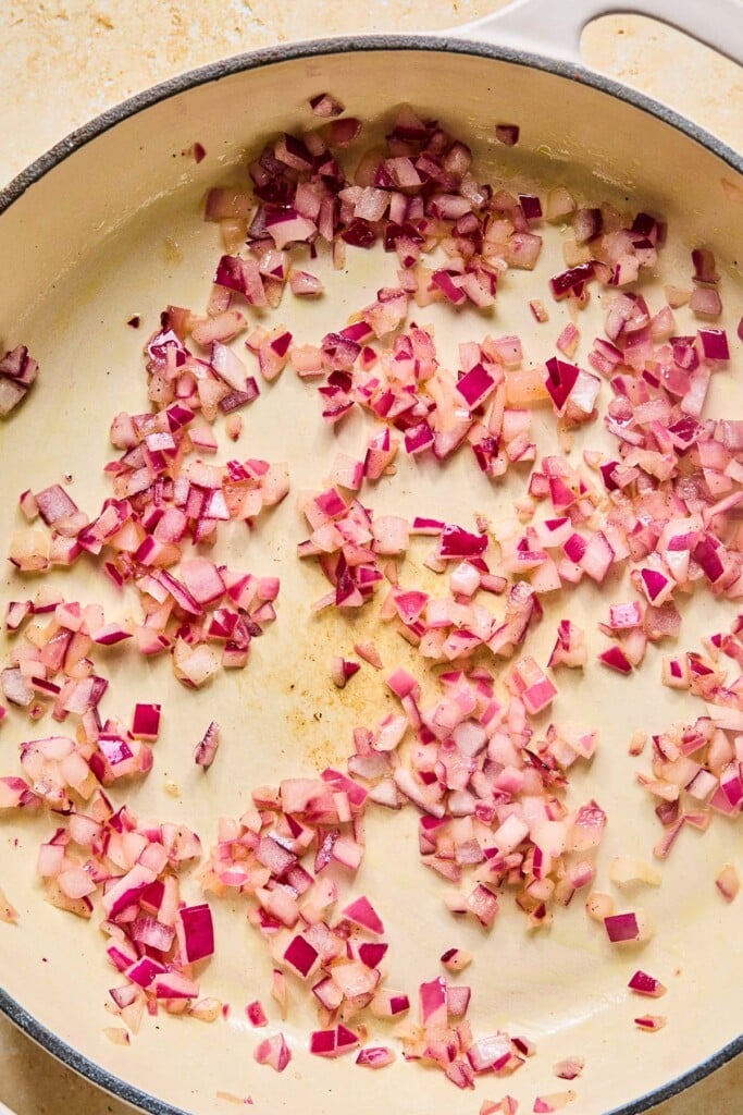 Large enameled pan filled with sautéed red onions.