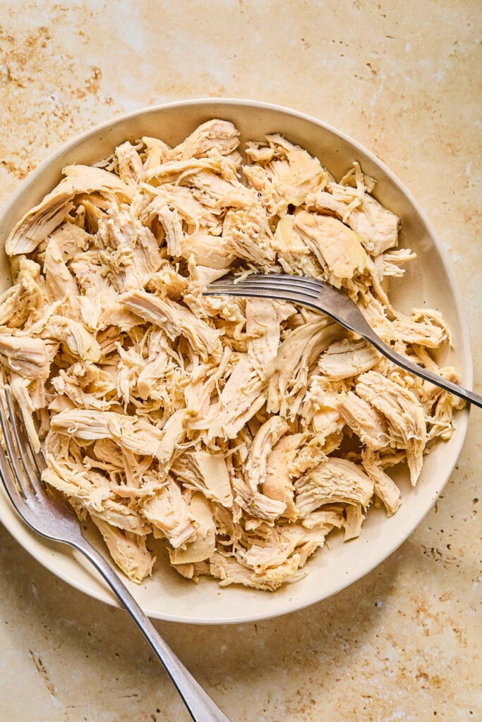 Large white bowl of shredded chicken with two forks in it.