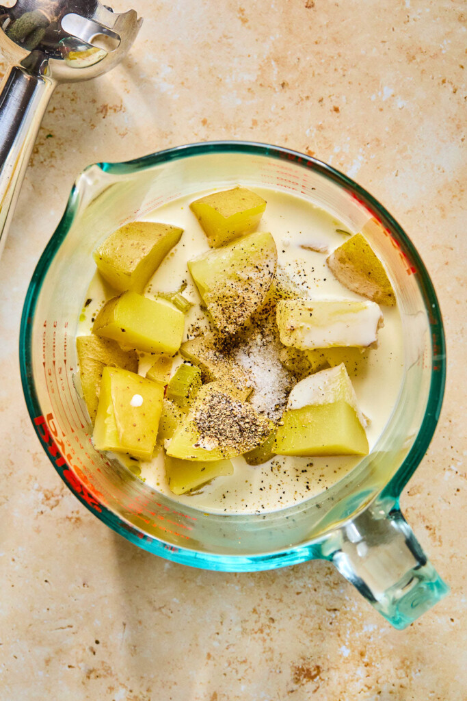 Measuring cup with cooked potatoes, a little broth, heavy cream, and salt and pepper in it.