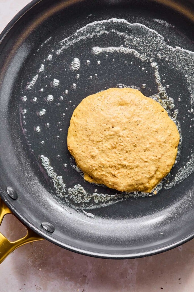 Large greased skillet with a greek yogurt protein pancake cooking on it before it is flipped.