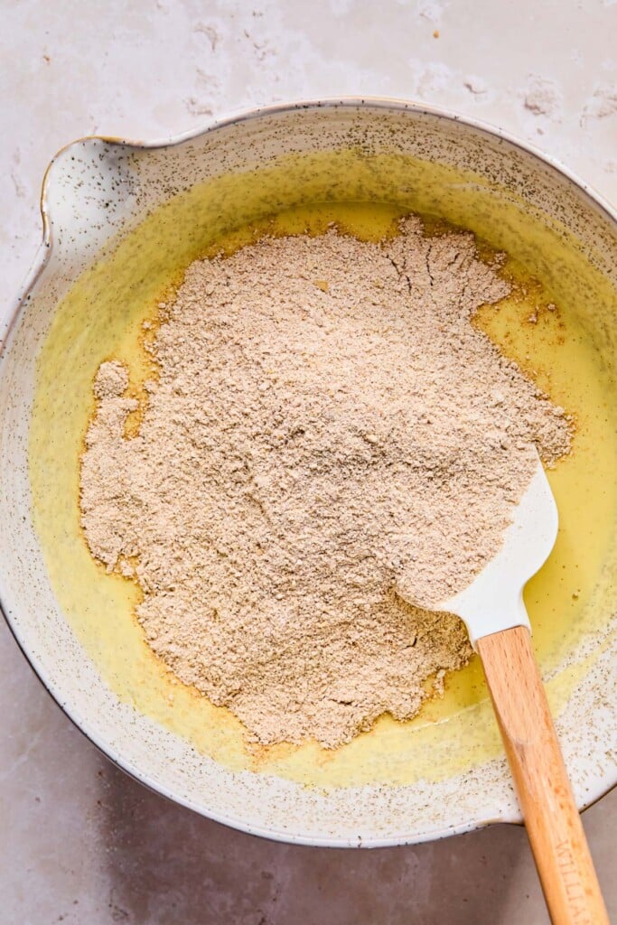 A mixing bowl with dry ingredients on top of a wet batter before it is mixed. A spatula is also in the bowl.