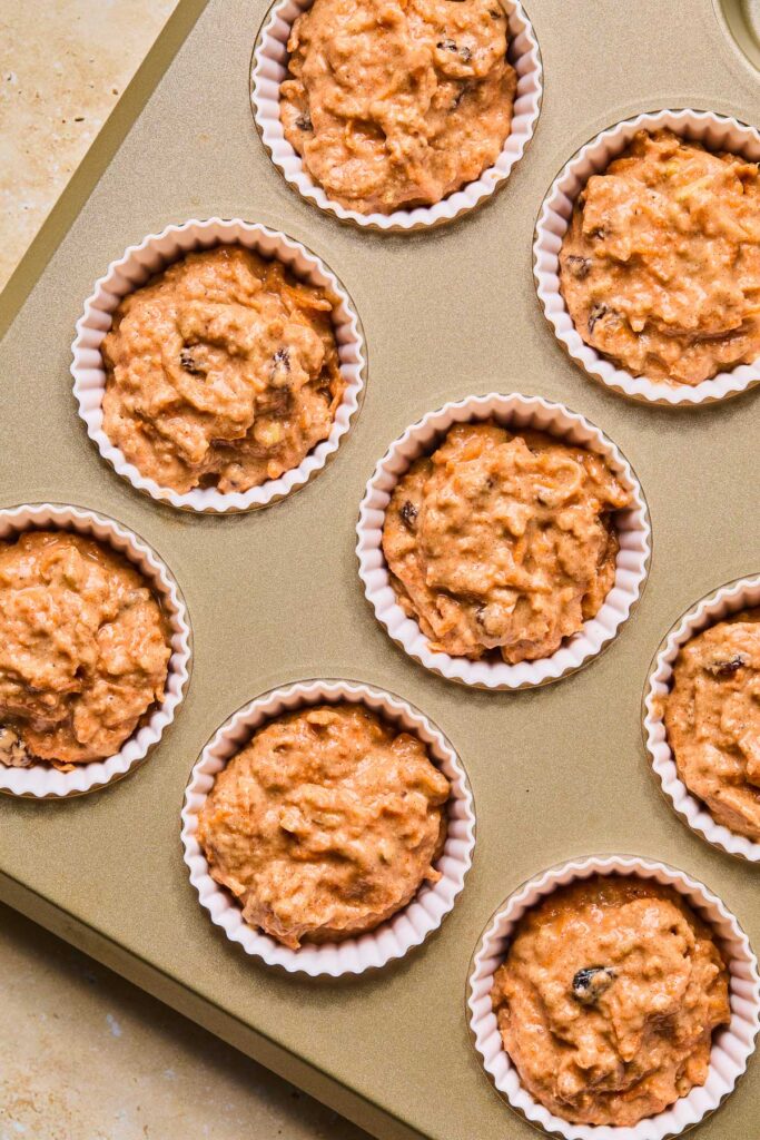 Carrot cake muffin batter in white liners in a muffin tin before it is baked.