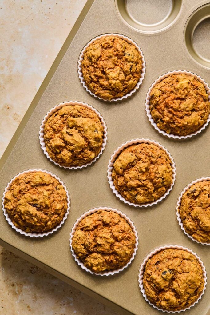 Healthy carrot cake muffins in white silicone liners in a muffin tin after they were baked.
