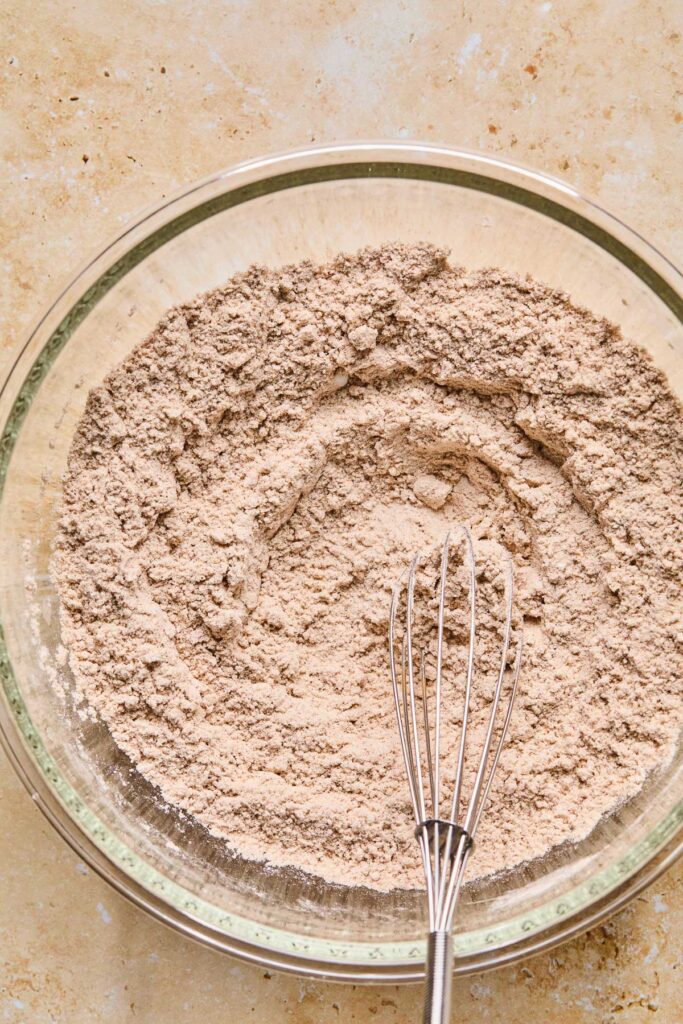 An overhead shot of a mixing bowl with flour and spices mixed together. A whisk is also in the bowl.