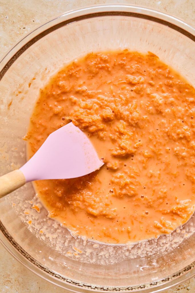 A wet batter with grated carrots in a bowl with a spatula in it.