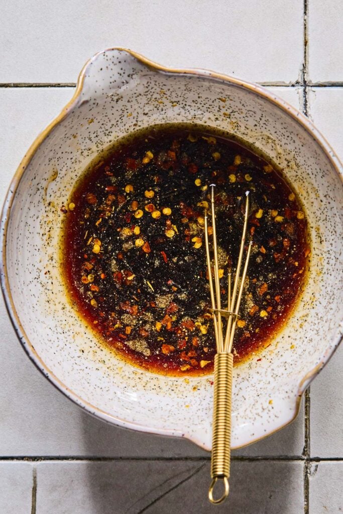 Bowl of stir fry sauce with red pepper flakes and a whisk in it.