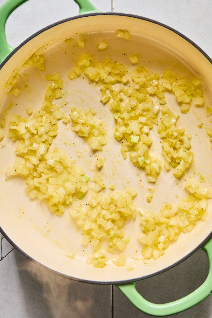 Large enameled pan filled with sautéed onions and garlic.