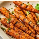 Grilled carrots on a serving platter topped with chopped cilantro. Around the platter is more fresh cilantro.